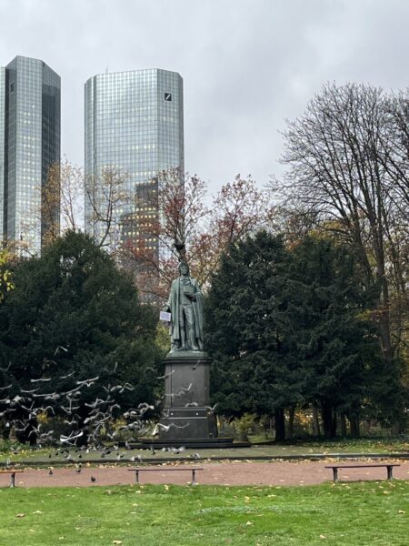 statue in park with birds and buildings